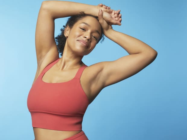 Photo of woman raising arms above head against blue background