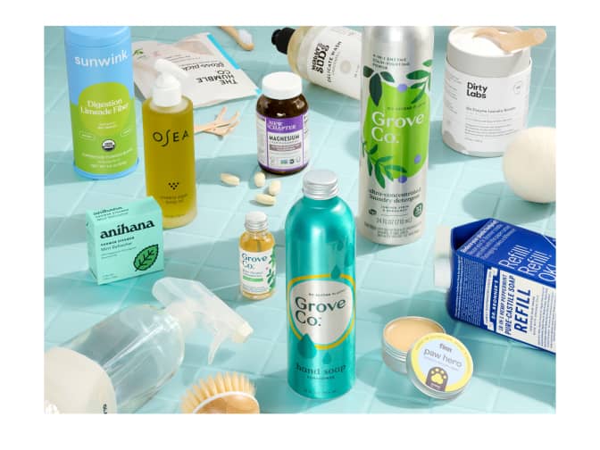 Collection of Grove products on a blue tile surface. Products include aluminum hand soap refill, aluminum packaged liquid laundry detergent, glass bottle of multivitamins, cleaner concentrate with a refillable glass spray bottle, and more.
