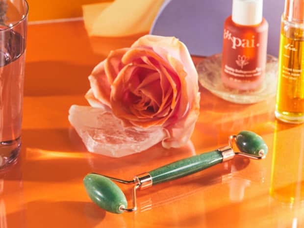 Photo of jade roller on orange table with rose and serums