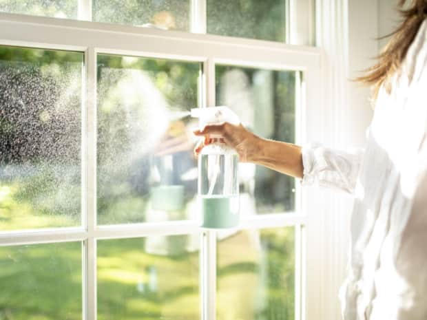 Person spraying glass window with cleaner