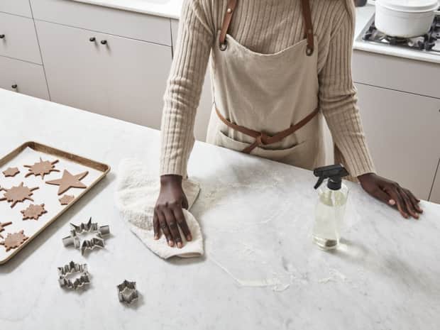 Photo of woman wiping flour off of counter with tray of cookies on it