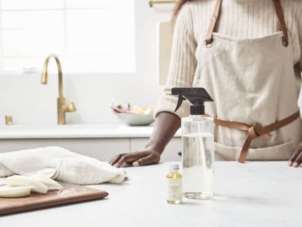 Woman in kitchen with spray bottle and essential oil on counter