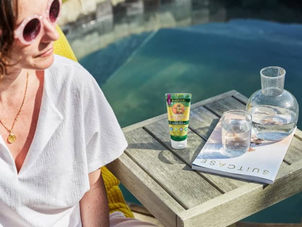 woman sitting next to a pool or something with a bottle of badger sunscreen SPF sun screen water