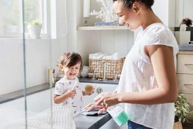 young child in bathtub playing while woman cleans the ledge of the bathtub