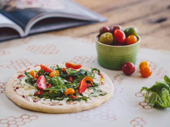 Image of a pizza on bees wrap next to tomatoes in a cup