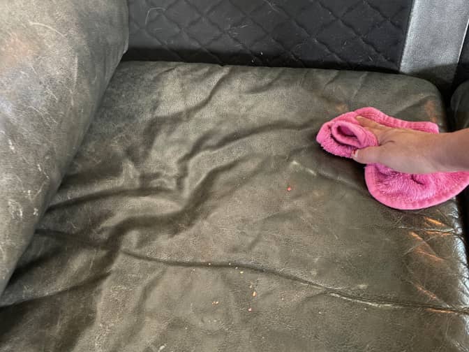 Someone wiping the dust from a leather couch with a microfiber cloth.