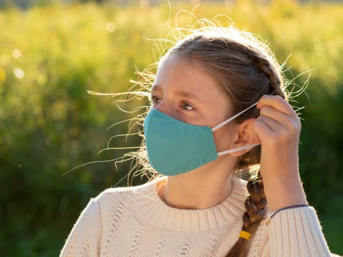 Image of girl in braids putting face mask strap behind her ear