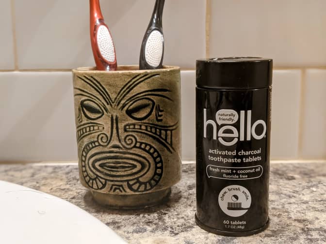 Photo of toothbrush holder with two toothbrushes and Hello Activated Charcoal tooth tablets next to it