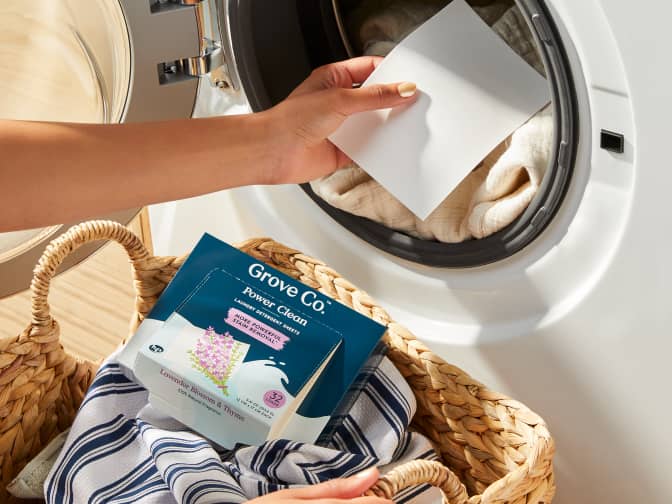 Image shows a person putting a Grove Co. Laundry detergent sheet into the washing machine.