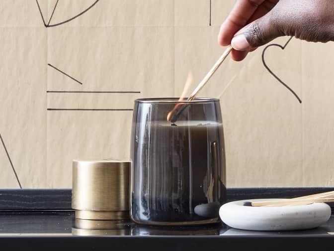 Image of someone lighting a candle in dark grey glass with match stick
