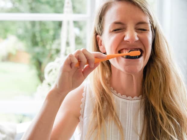 woman brushing her teeth with natural toothpaste and a toothbrush