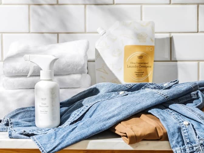 Product image of Grove Stain Remover Spray and laundry detergent on top of laundry