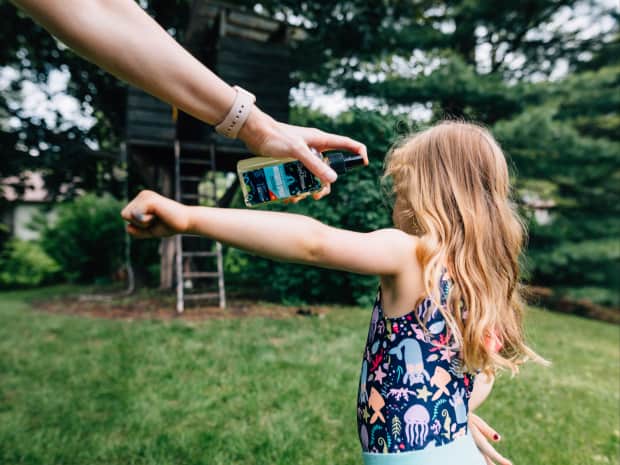 Little girl outside in bathing suit getting sprayed with insect repellent by parent