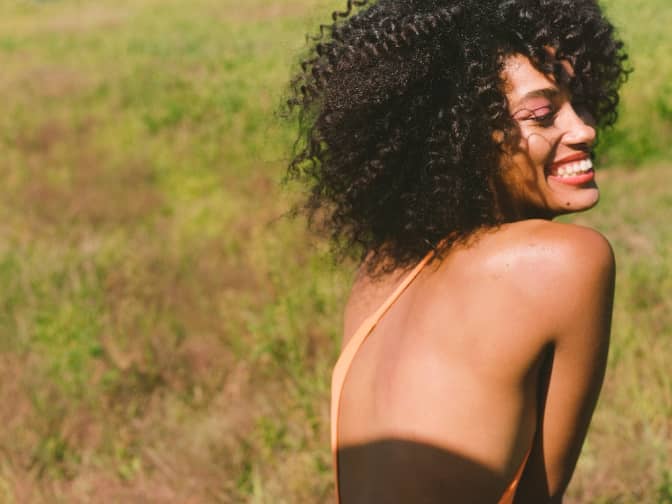 woman looking over her back smiling in the sun.