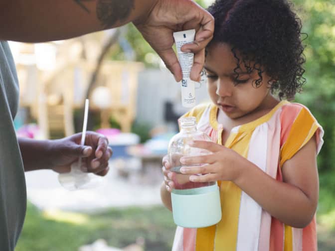Parent pouring cleaner concentrate into glass bottle that child is holding