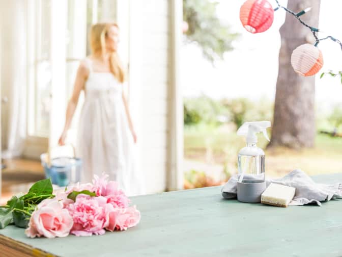 Image of woman in white dress in background standing next to open door with roses and string lights in foreground