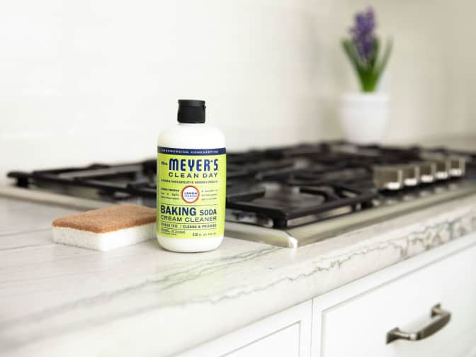 Image of Mrs Meyer's Cream Cleaner bottle on countertop next to range and walnut scrubber sponge