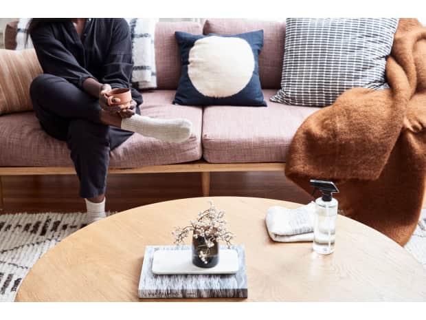 Woman drinking coffee sitting on couch with spray bottle on table