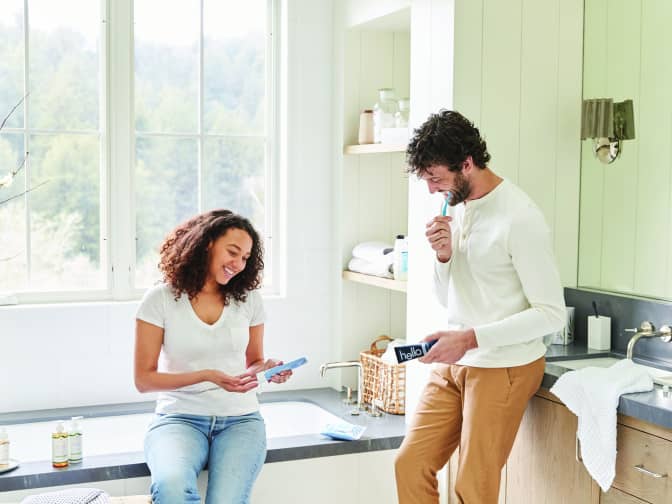woman putting on lotion and man brushing teeth in bathroom