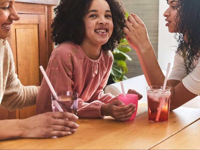 family drinking juice fro cups with silicone straws around a wooden dining table