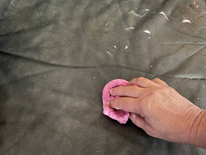 A hand scrubbing dish soap softly into a leather couch.