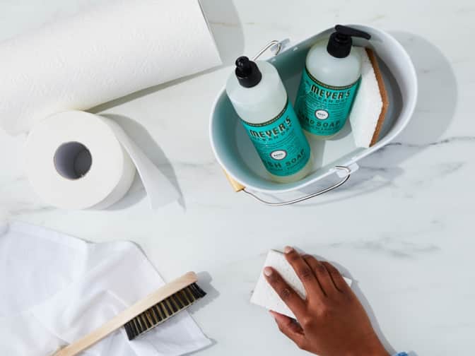 Hand wiping countertop next to cleaning supplies