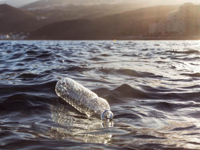 An empty plastic water bottle floats in a lake by the hills
