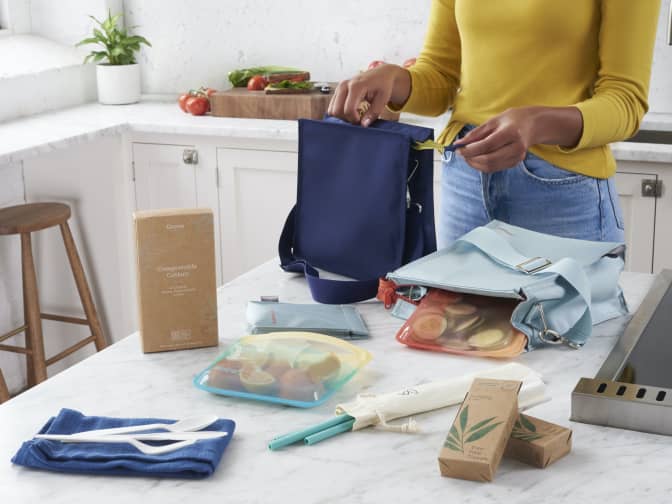 Image of a woman packing a lunch on a countertop with zero waste tools from Grove including a reusable lunch pack, reusable straws, stasher reusable bags, compostable cutlery, and tree-free tissues.