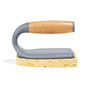 The Tub Handler + Residue Remover by Grove Co. features a scrub brush with a bamboo handle, standing upright on its gray holder and yellow sponge base.