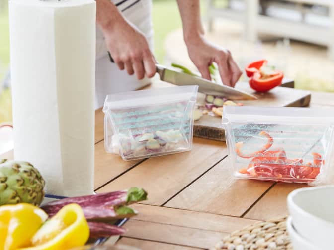 person chopping vegetables on a cutting board to place in reusable food bags